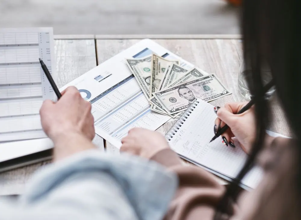 Persona contando billetes mientras anota cuentas en un cuaderno