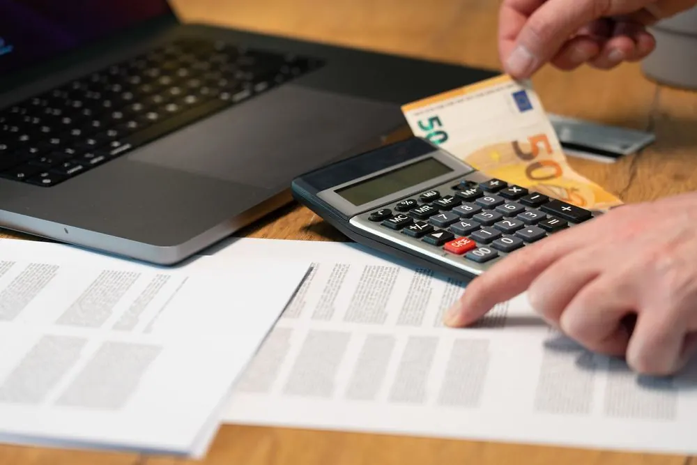 Manos con una calculadora y un billete de 50 euros junto a un portátil