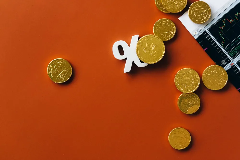 Monedas de euro y un símbolo de porcentaje sobre fondo naranja junto a una gráfica de mercado
