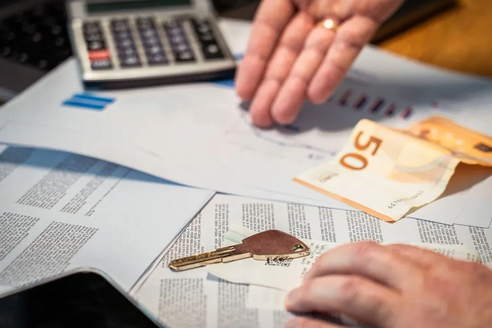 Manos sobre documentos de hipoteca con una calculadora, billetes y una llave de casa