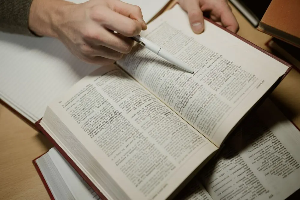Libro abierto mientras alguien señala una línea con un bolígrafo