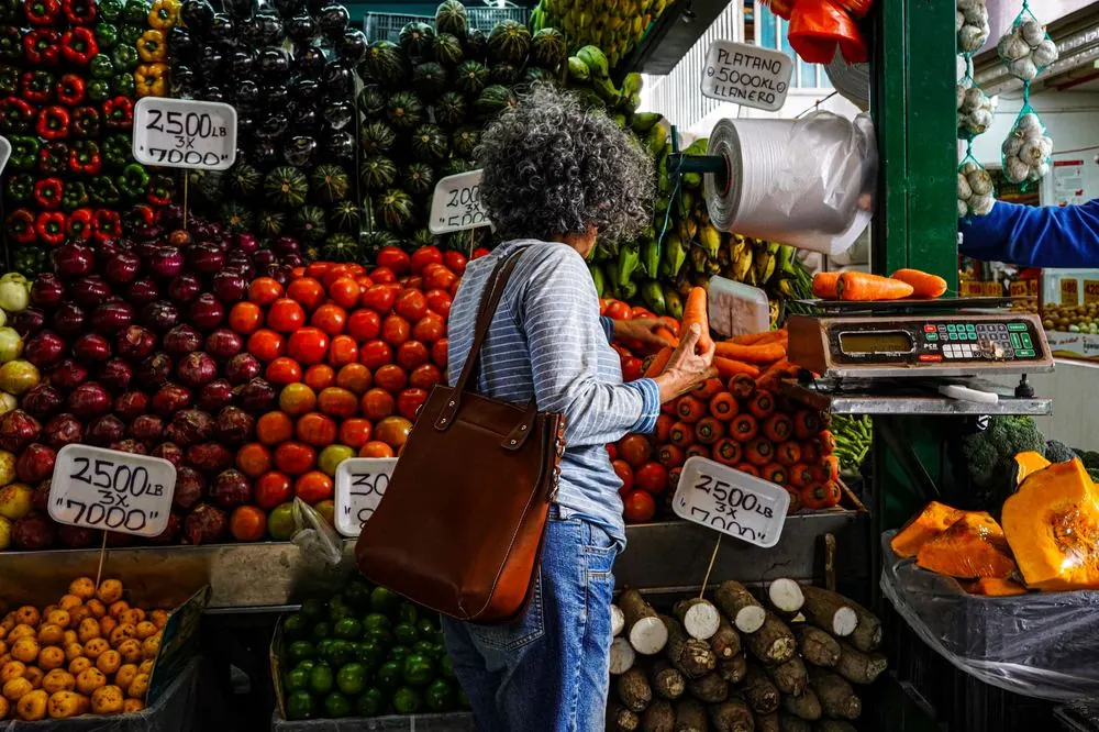 Mujer comprando en un puesto de fruta y verdura con los precios a la vista
