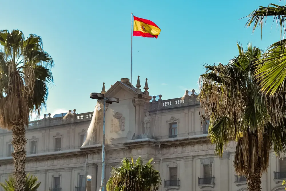 Bandera de España ondeando sobre un edificio histórico entre palmeras